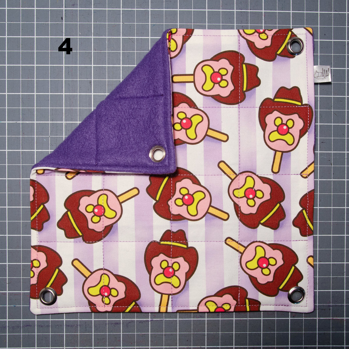 Flat lay photo of a small flat rat hammock with bubble o bill fabric on one side and purple fleece on the other side with grommets in each corner. There is a number 4 in the left top corner.