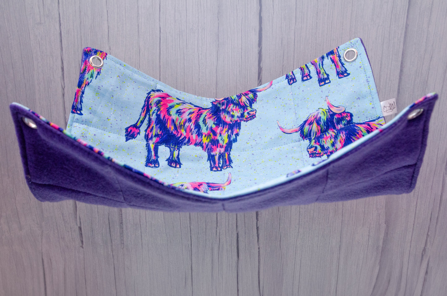 Trippy cows fabric in a flat hammock style, hanging with purple fleece