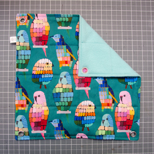 Flat hammock, flat lay, colourful birds in a mosaic pattern, folded corner to see underside made of fleece.