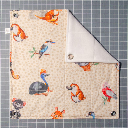 Photo of flat lay flat style hammock with fabric print showing a pale brown background with cartoon characters depicting koalas, platapus, tasmanian devils, emus, kookaburras, numbats and galashs.