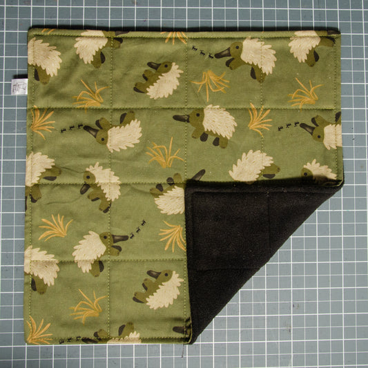 Fabric with echidna pattern on an olive green background, folded on a grid cutting mat