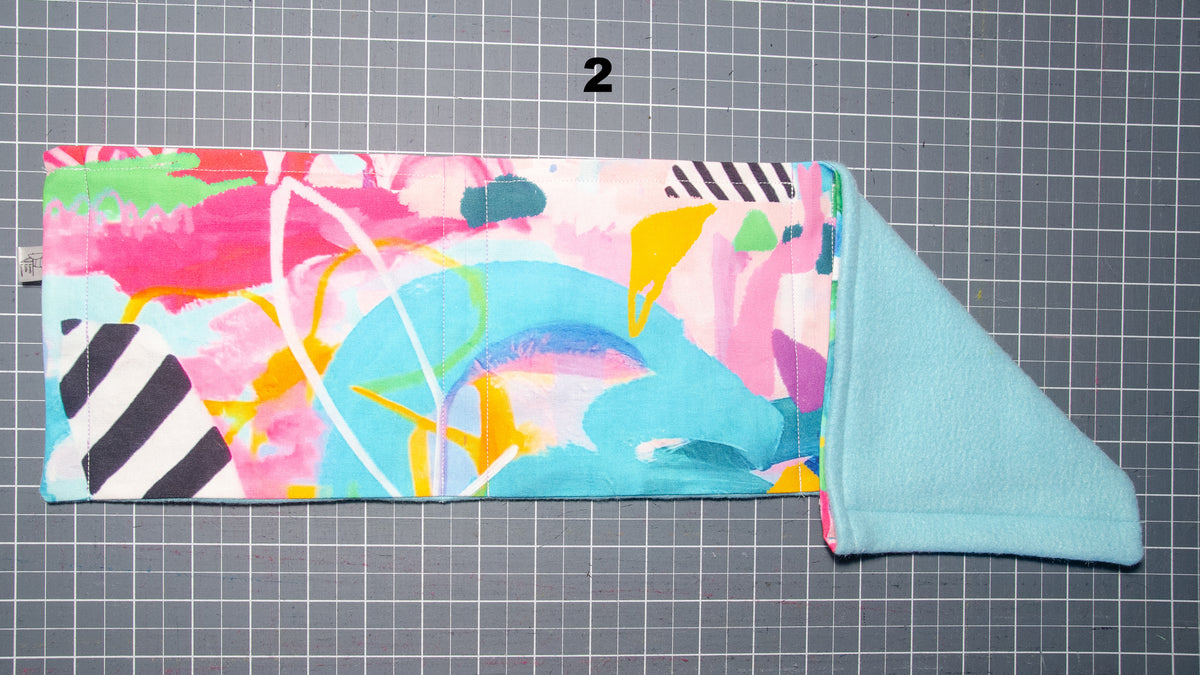 A flat lay image of a step hammock with a floral design folded on one side to show the colour of the fleece on the other side. Number 2 above the image.