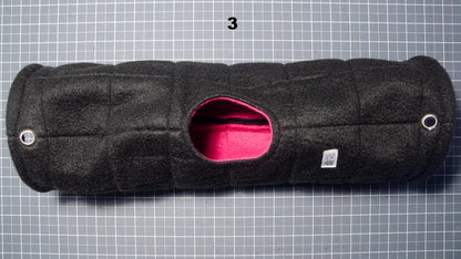 A black quilted fleece pet tunnel with a pink interior lining, shown from a top-down view on a gray grid cutting mat.